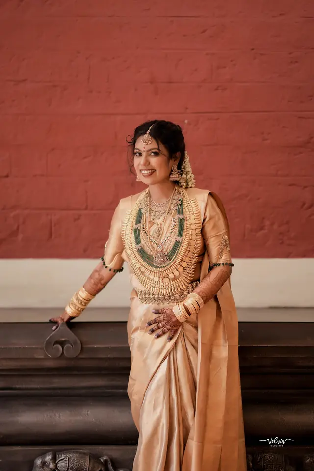 Bride in a gold tissue saree with a long layered necklace — makeup by Popyz Beauty Lounge, Kozhikode