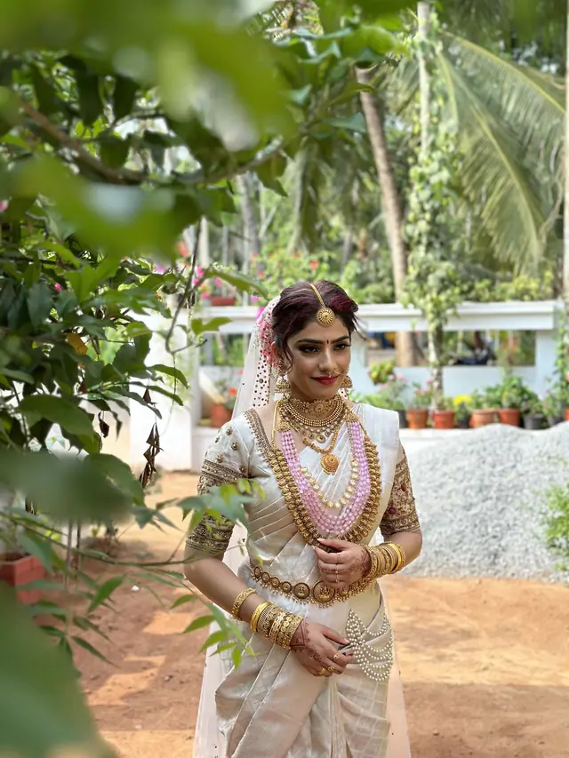 Kerala bride in a cream silk saree with gold jewellery and jasmine, outdoors — makeup by Popyz Beauty Lounge, Kozhikode