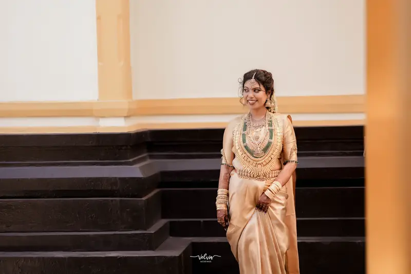 Kerala bride in a gold silk saree on a heritage verandah — makeup by Popyz Beauty Lounge, Kozhikode