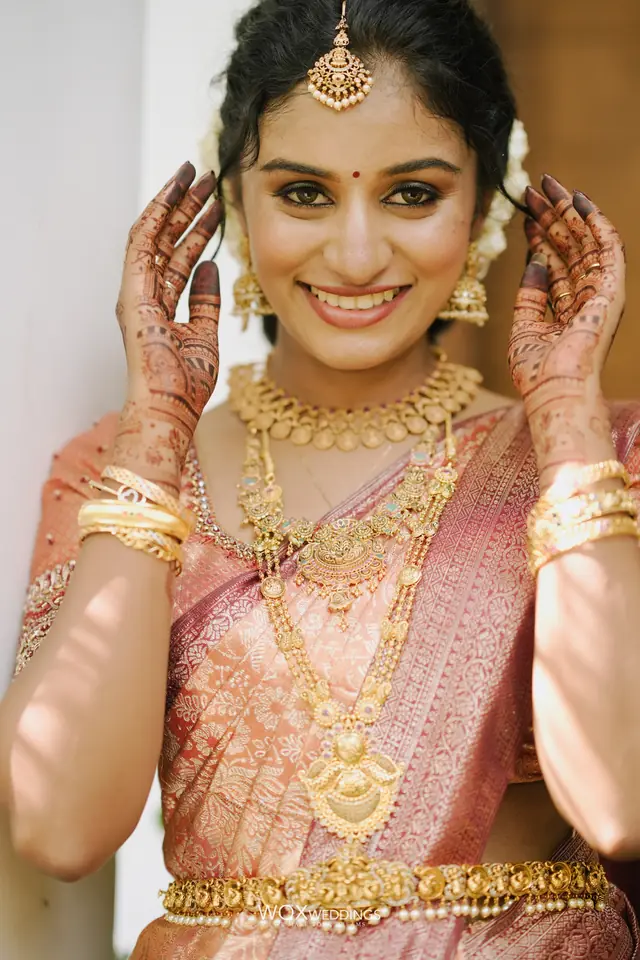 Smiling Kerala bride in a pink silk saree with gold jewellery and jasmine in her hair
