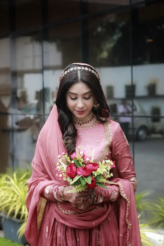 Bride in a dusty pink gown and veil holding a rose bouquet — makeup by Popyz Beauty Lounge, Kozhikode
