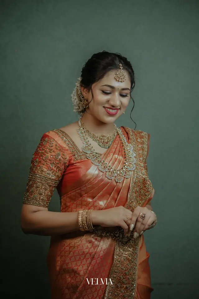 Kerala bride in an orange silk saree with gold jewellery, photographed after her bridal makeup at Popyz