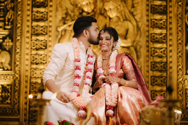 Bride and groom in front of a carved golden temple backdrop, bridal makeup by Popyz