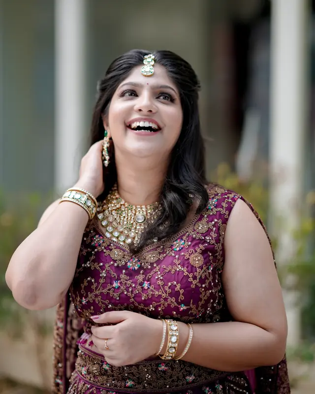 A woman laughing in a purple embroidered outfit with statement jewellery and soft glam makeup