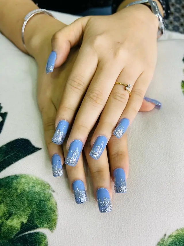 Hands with long periwinkle-blue nail extensions and one white accent nail