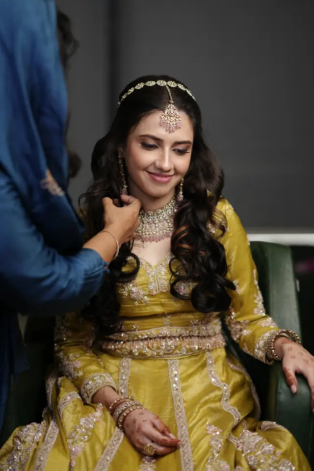 Bride in a mustard lehenga having her necklace set by the team