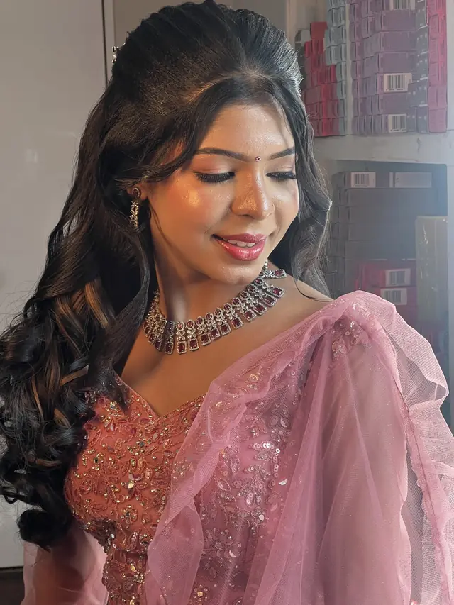 Woman in a pink net saree with soft curls and luminous, glowing makeup